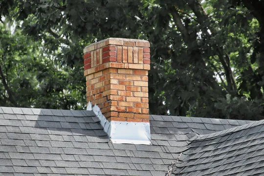 Brick chimney with a decorative top and metal flashing where it meets the roof